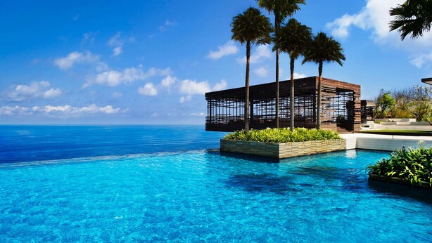 A clear blue pool with a wooden structure and palm trees, overlooking a calm sea. - Alila Villas Uluwatu, Bali (Pecatu)