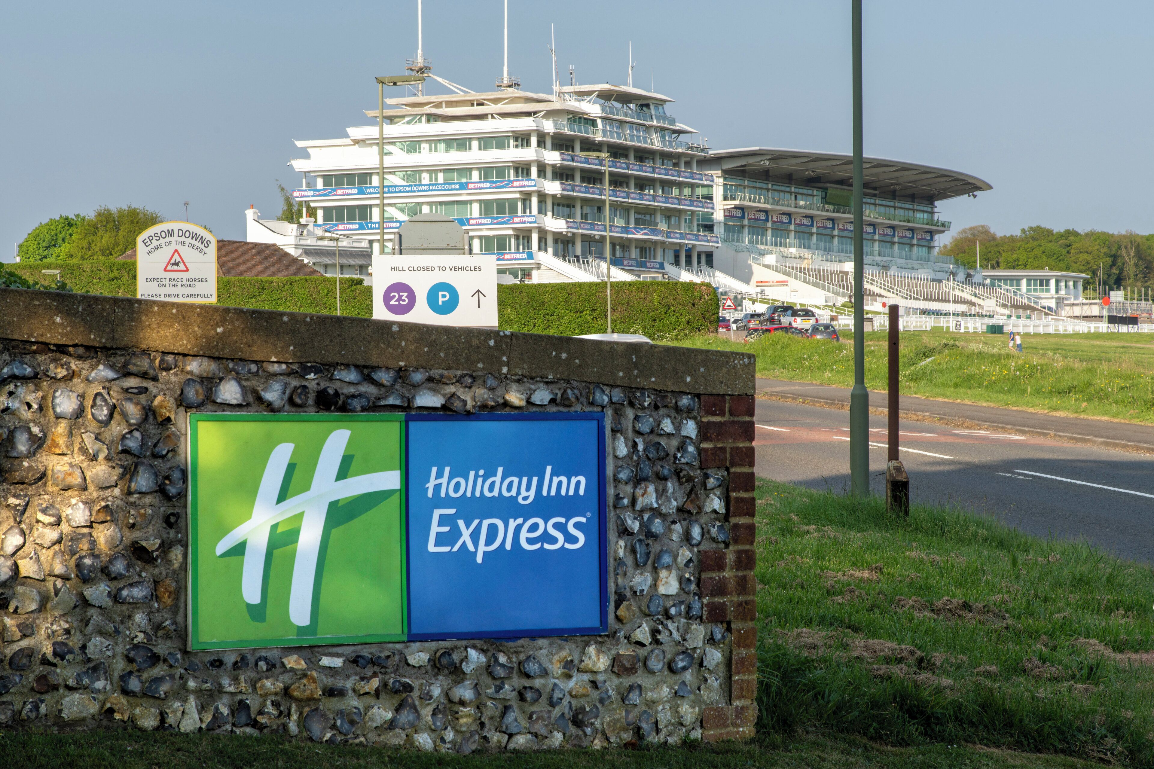 Placa do Holiday Inn Express com uma parede de pedra e um edifício grande ao fundo.