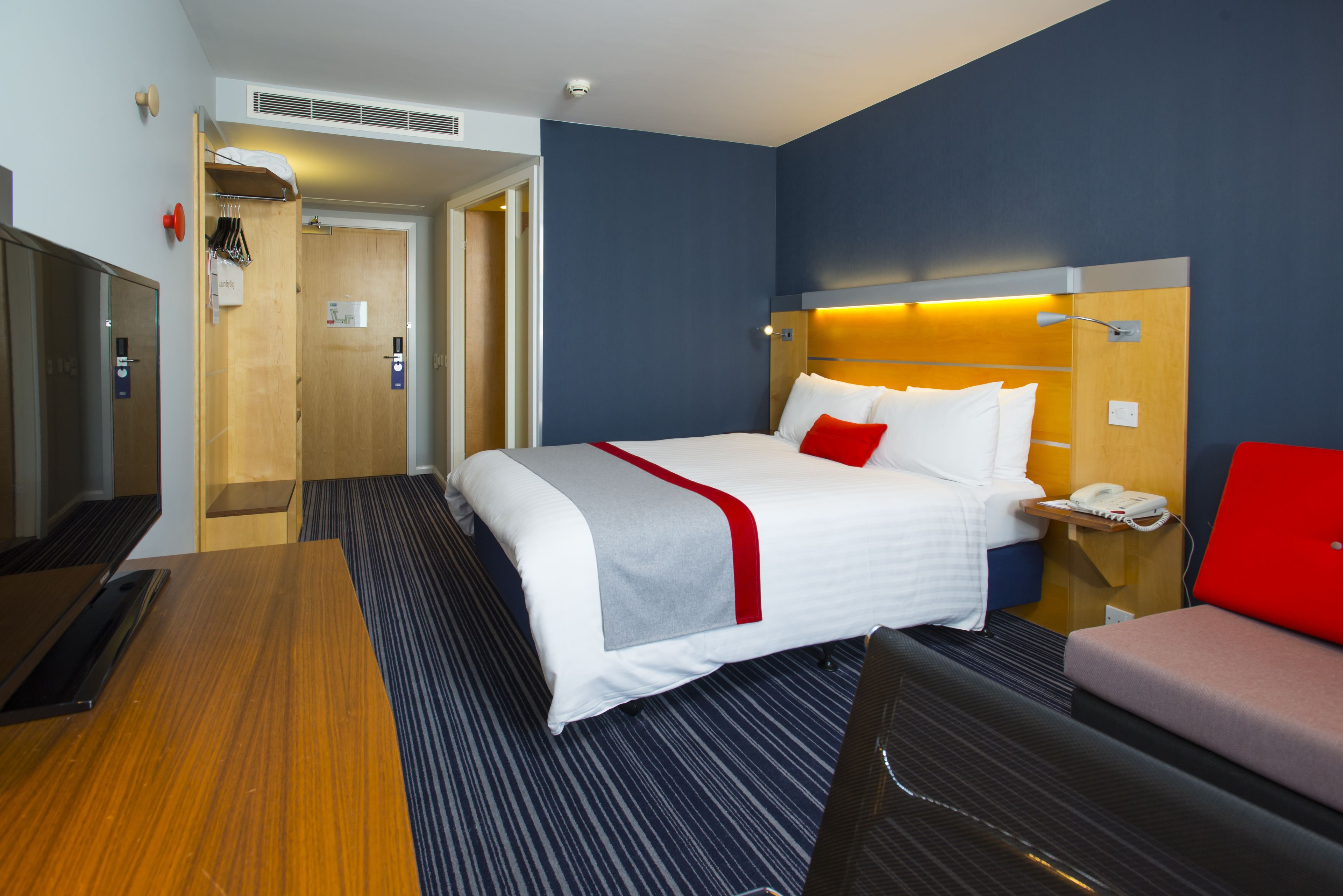 A hotel room with a bed, a desk, a chair, a TV, and a bathroom.