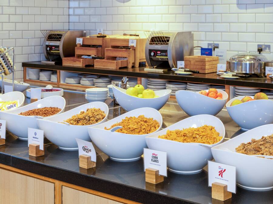 Un bufé con diversos alimentos en recipientes, incluyendo cereales, frutas y frutos secos.