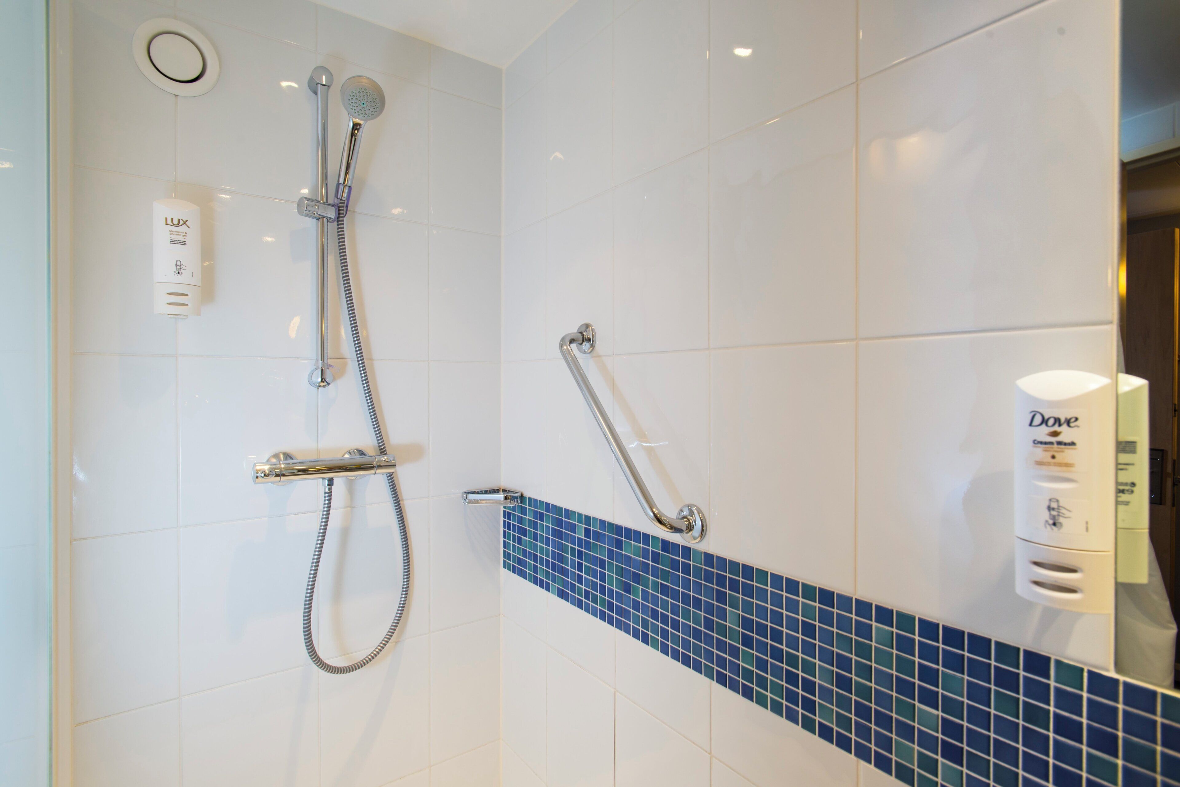 A bathroom with a shower, a hand dryer, and a soap dispenser.