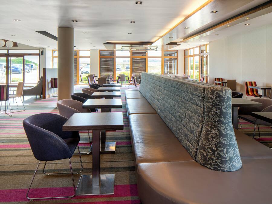 Un restaurante moderno con una barra larga, asientos acolchados y amplias ventanas con vistas al estacionamiento.