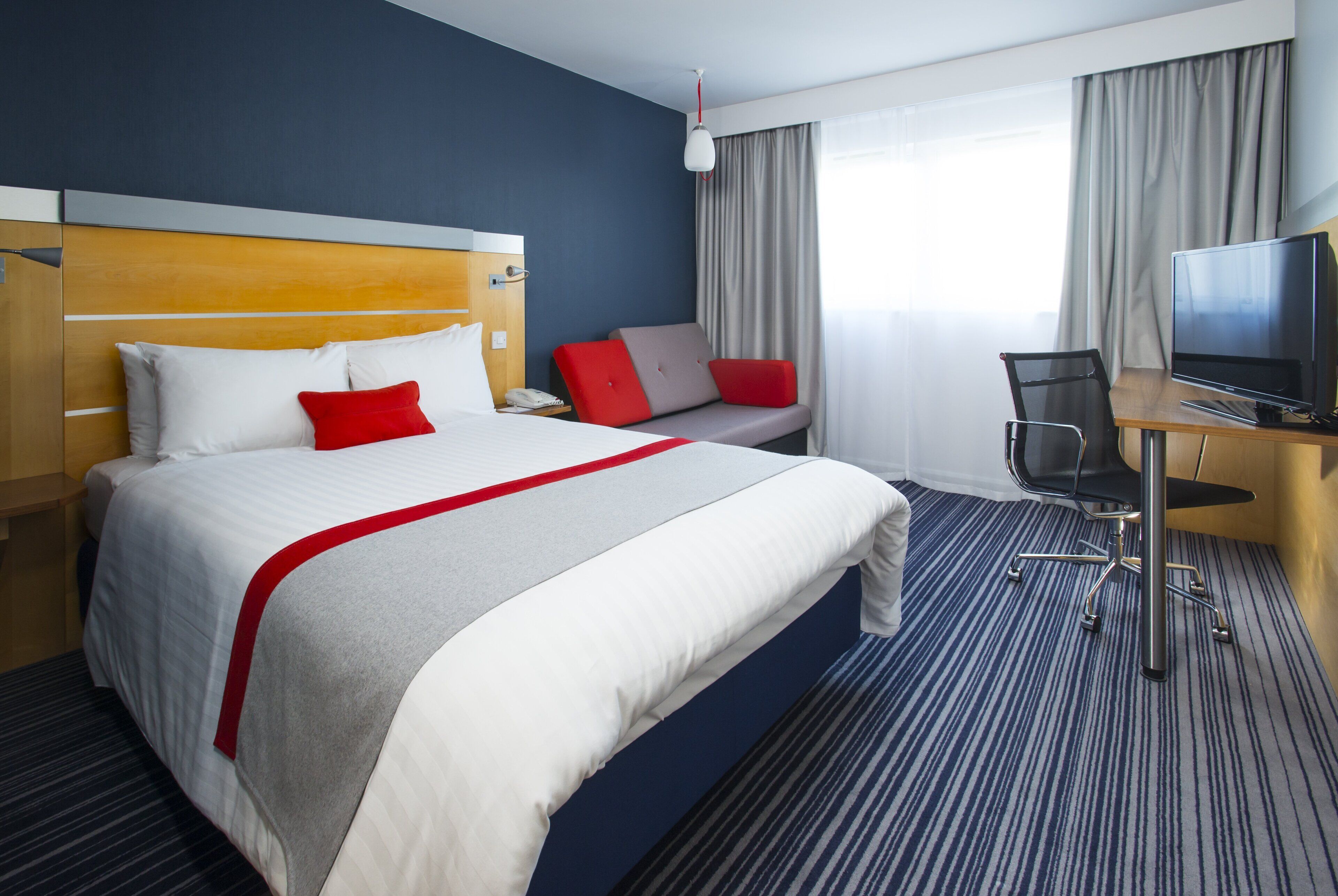 Een hotelkamer met een bed, bureau, stoel, televisie en een raam met gordijnen.