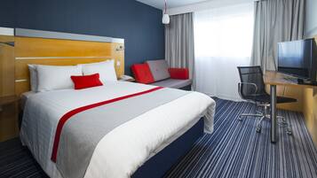 Een hotelkamer met een bed, bureau, stoel, televisie en een raam met gordijnen.