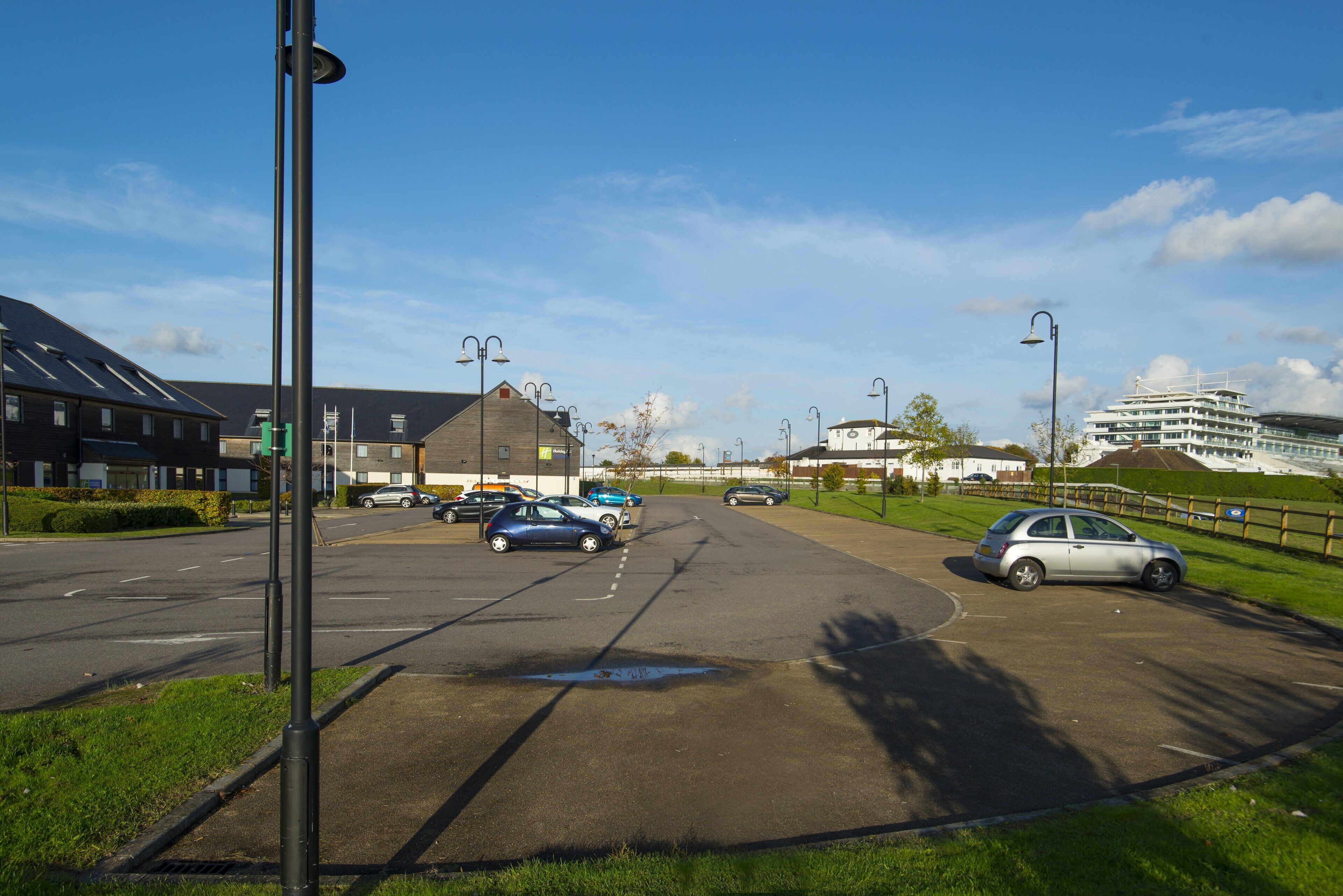 A parking lot with several cars, a pedestrian crossing, and buildings in the background.