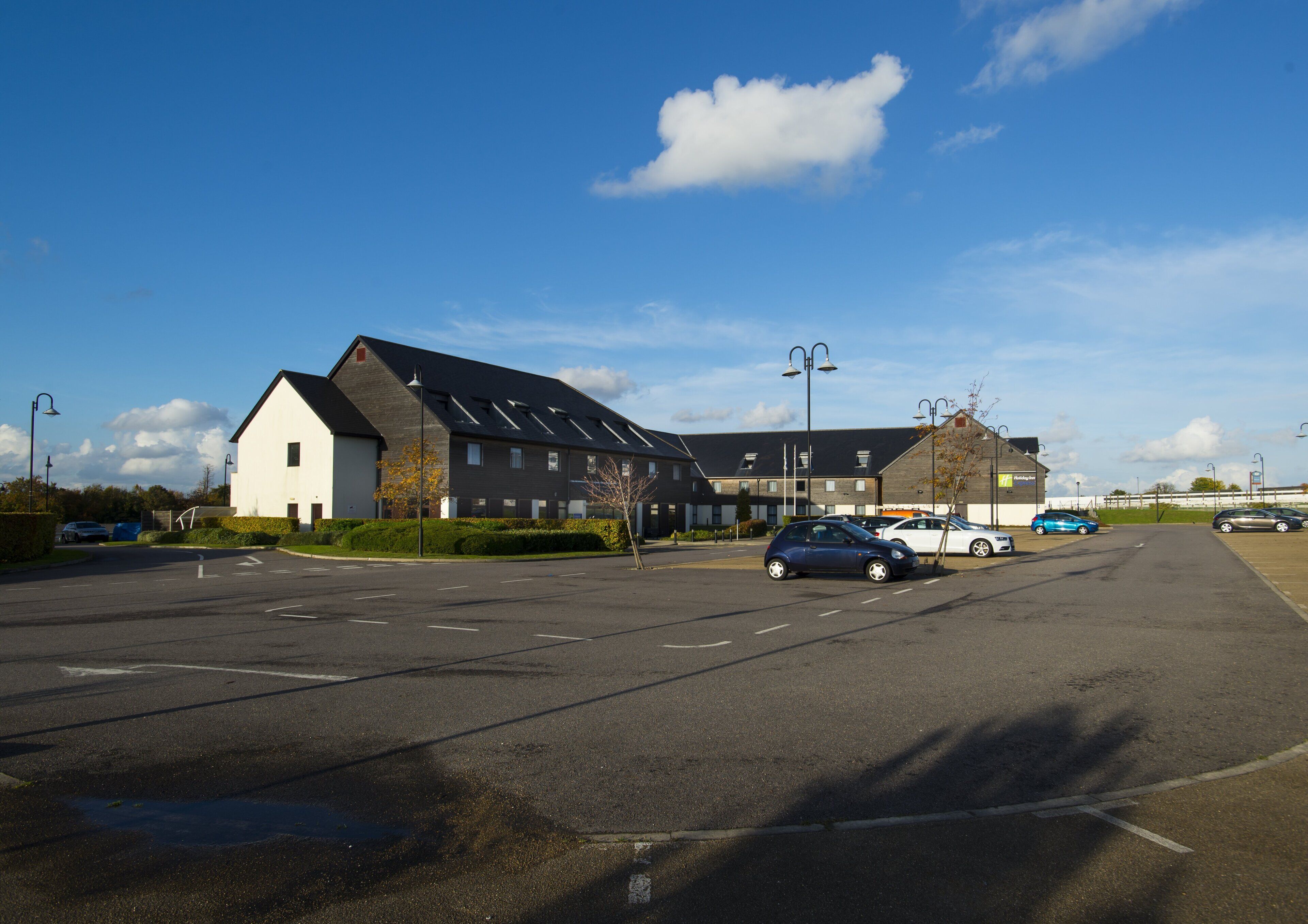 A parking lot with several cars, a building with a sloped roof, and a clear blue sky.