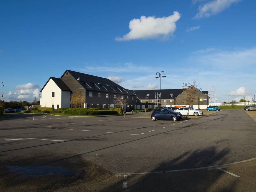 A parking lot with several cars, a building with a sloped roof, and a clear blue sky.