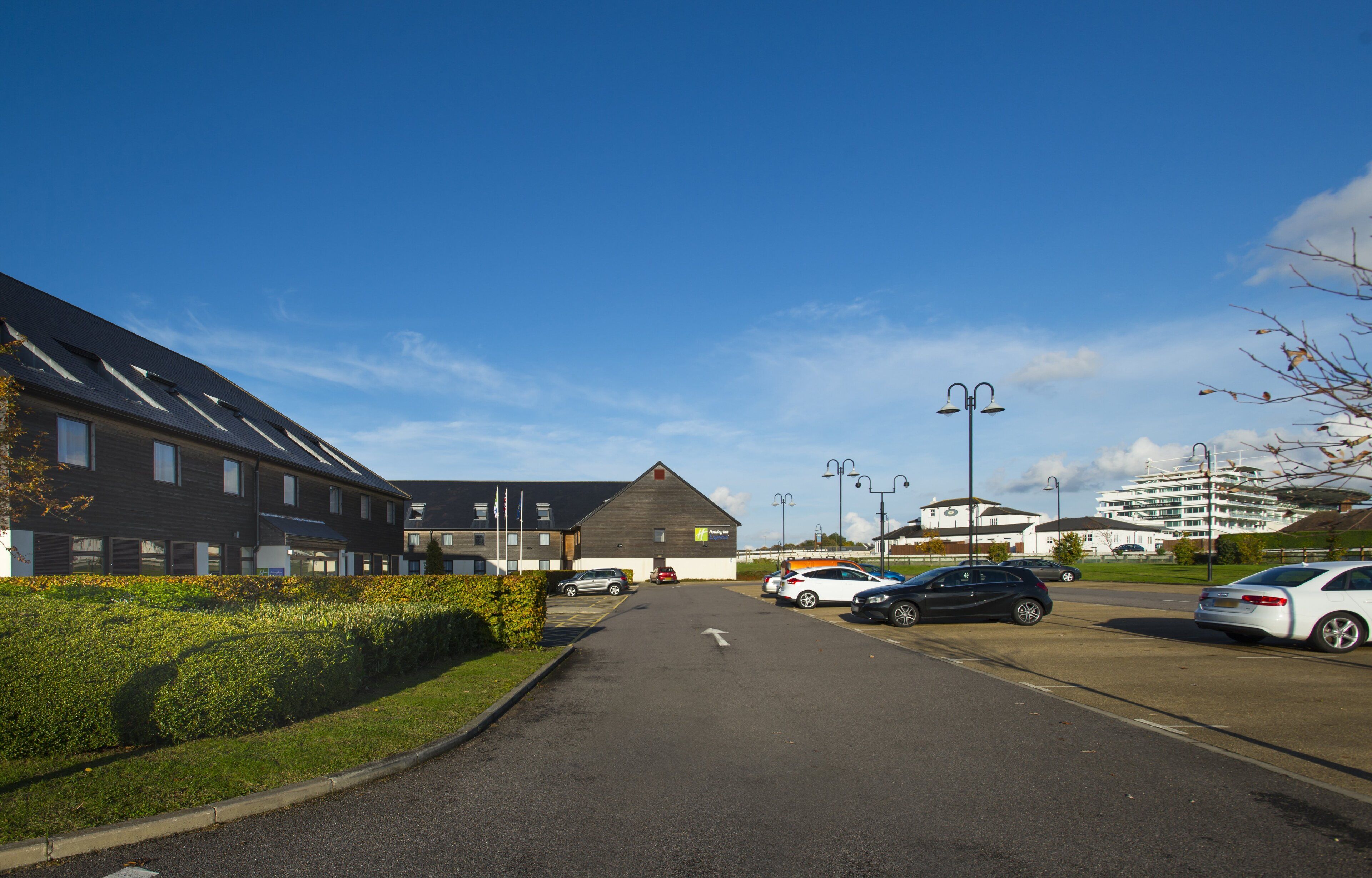 A parking lot with cars, a building with a sloped roof, and a clear blue sky.