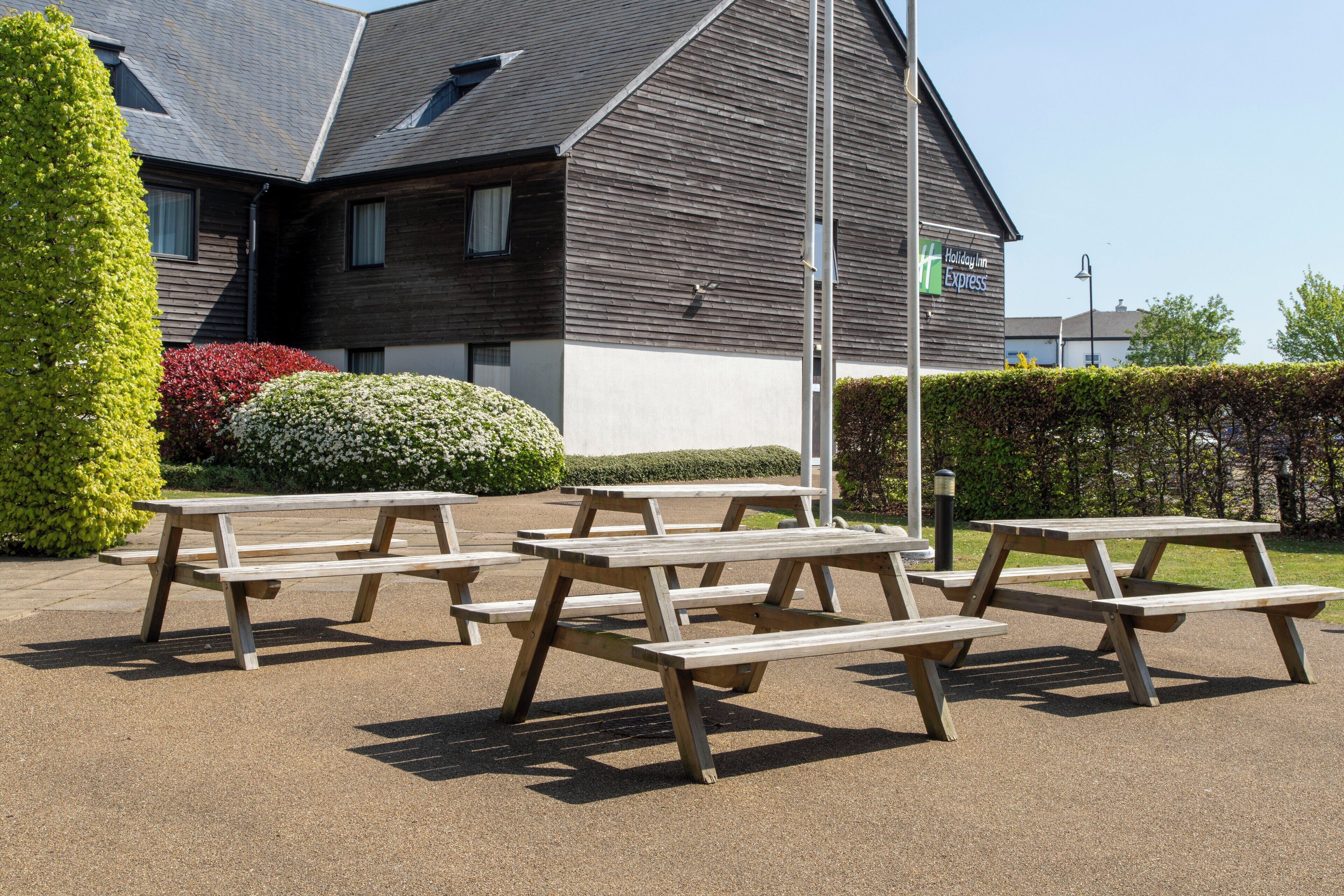 A Holiday Inn Express with outdoor picnic tables and a building with a sloped roof.
