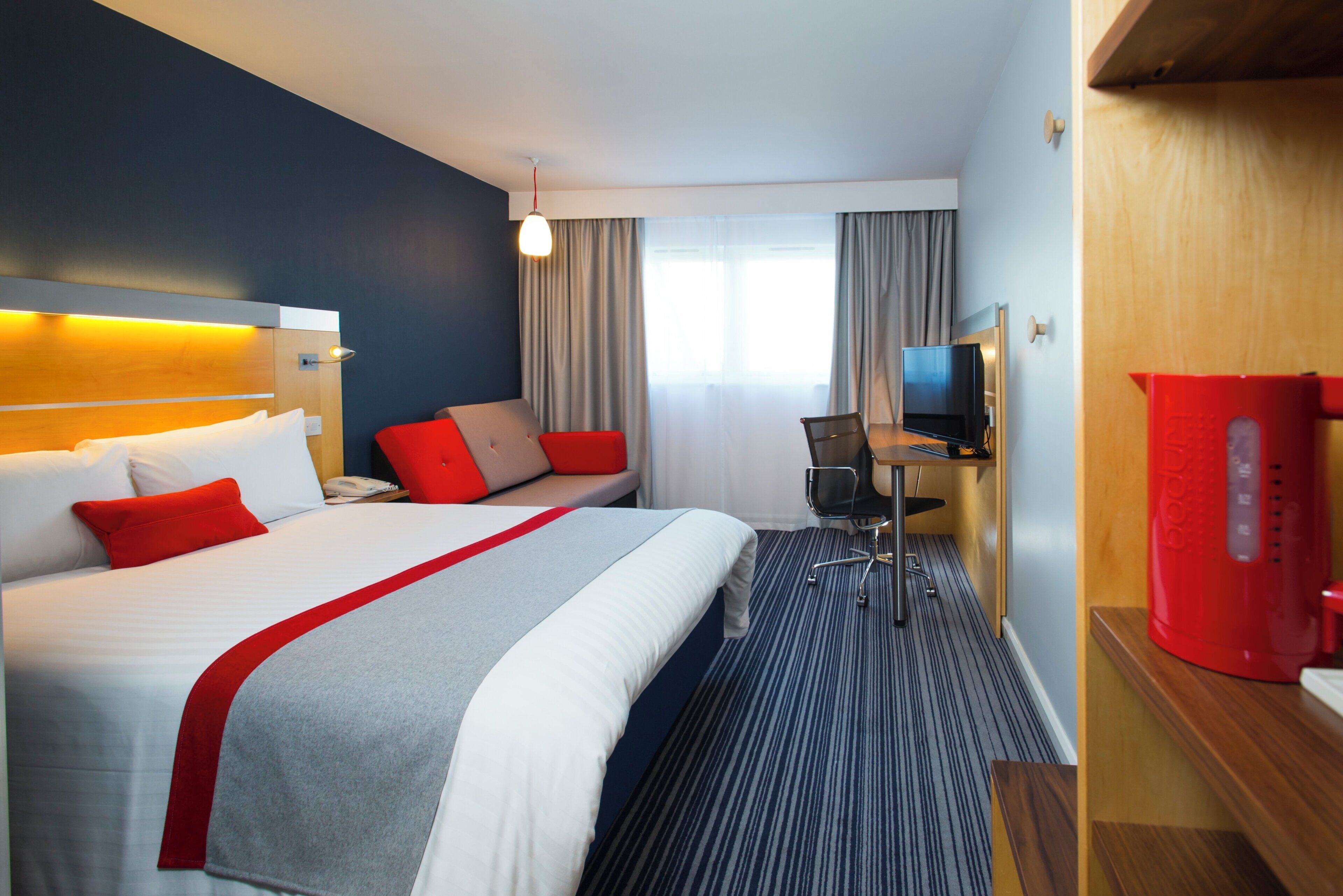 Een hotelkamer met een bed, een bureau, een stoel, een televisie en een rode speaker.