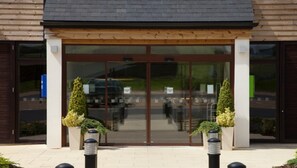 A building entrance with a glass door, two potted plants, and a paved walkway. - Holiday Inn Express London-Epsom Downs by IHG (Epsom)