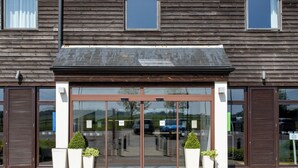A building entrance with a glass door, potted plants, and a paved walkway.