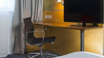 Habitación de hotel con cama, escritorio, televisor, una silla y ventana con cortinas.