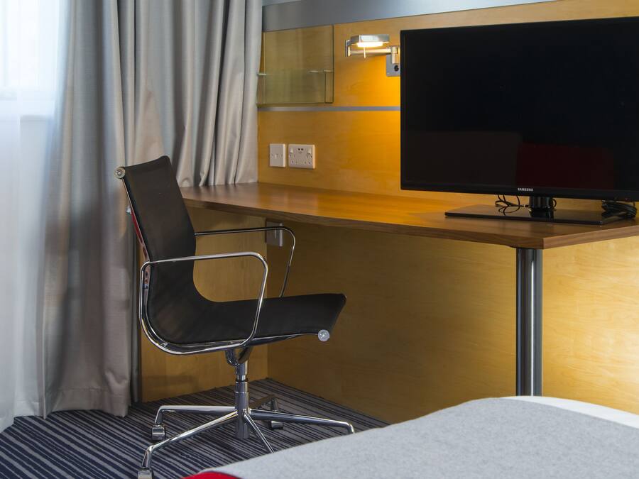 Habitación de hotel con cama, escritorio, televisor, una silla y ventana con cortinas.