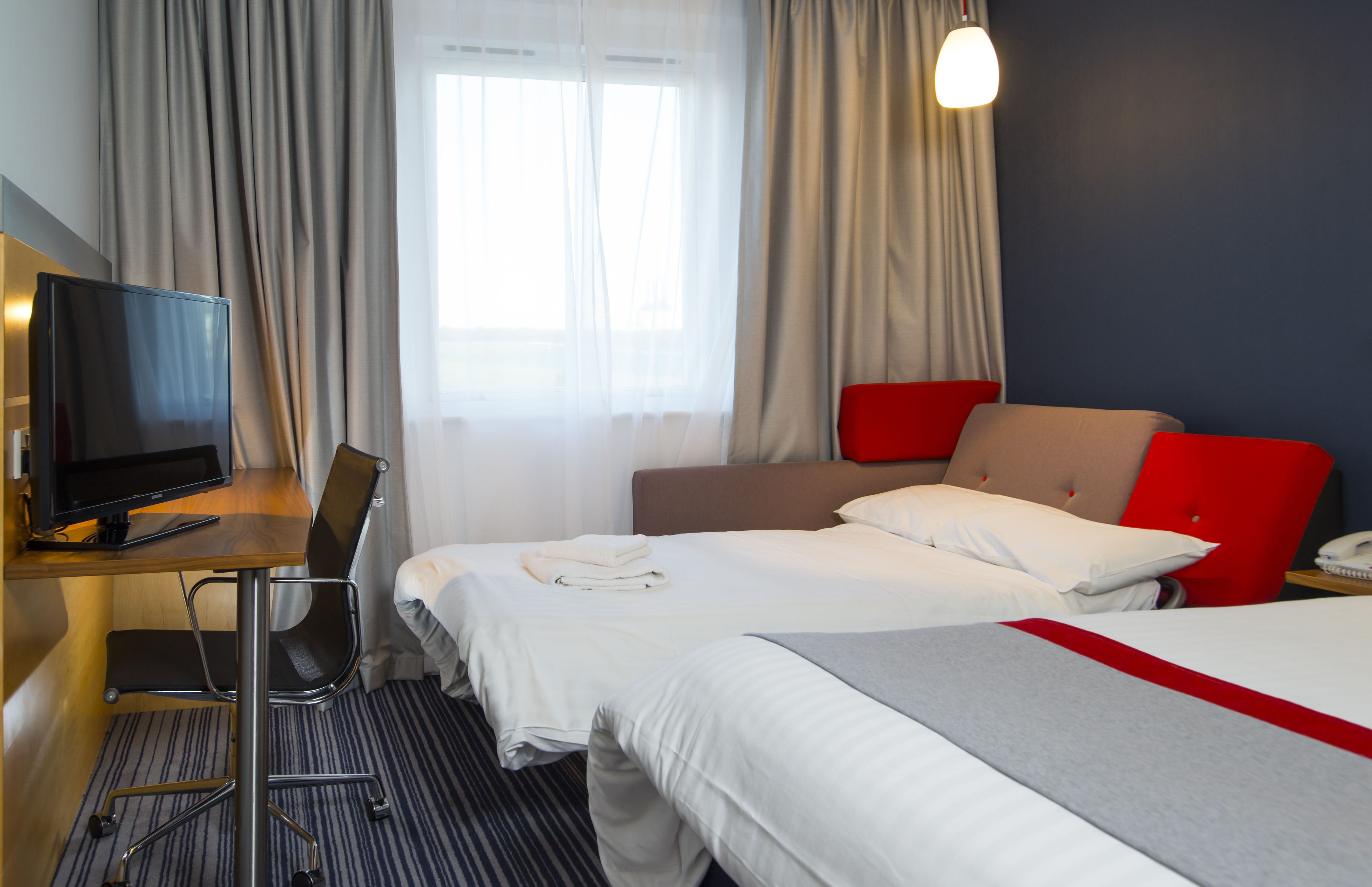 Una habitación de hotel con dos camas, un escritorio con computadora, una silla y un televisor.