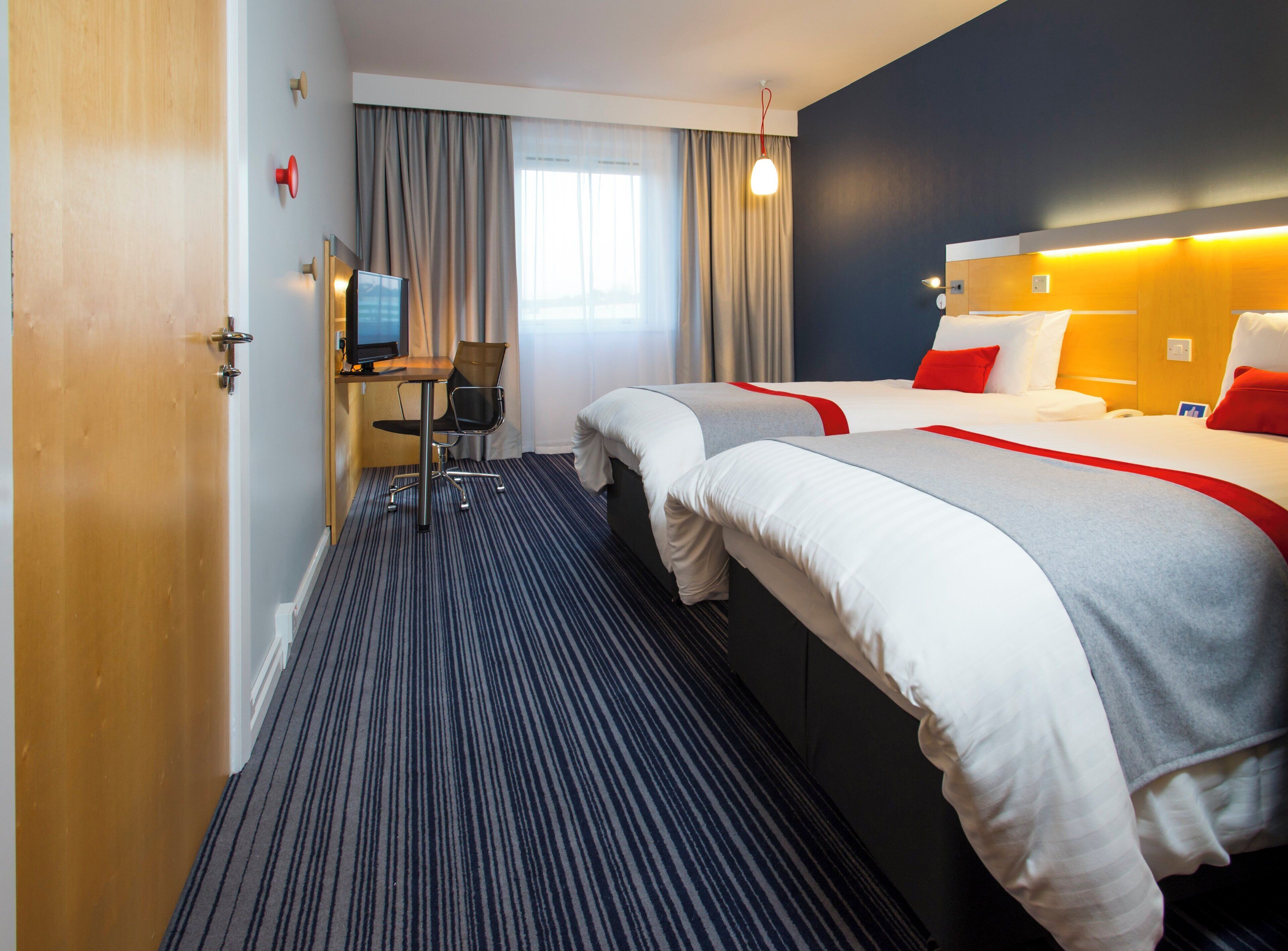 Quarto de hotel com duas camas, uma escrivaninha, uma cadeira e uma televisão.