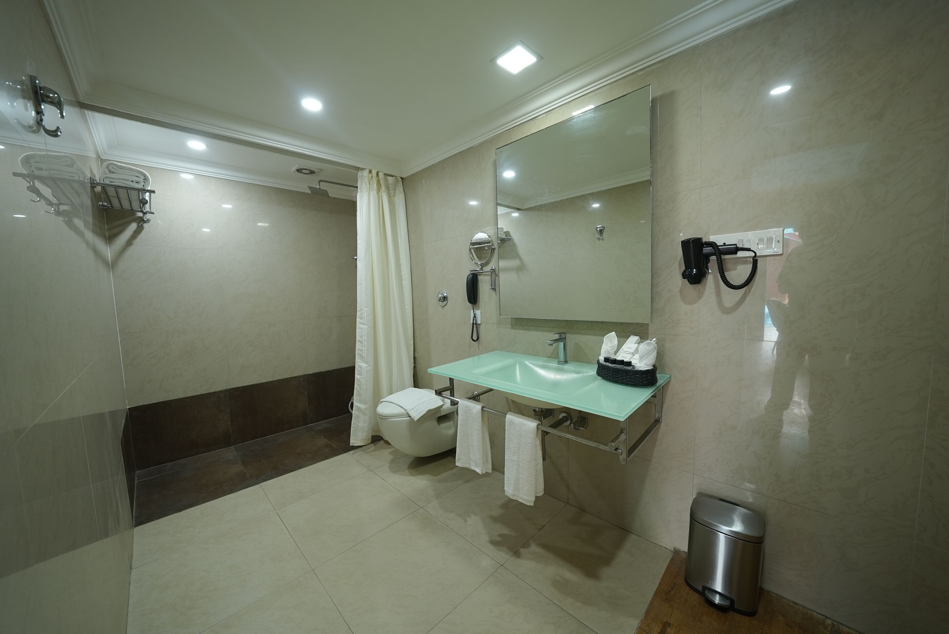 Une salle de bain moderne avec un lavabo en verre, un miroir, un porte-serviettes, une douche et une poubelle.