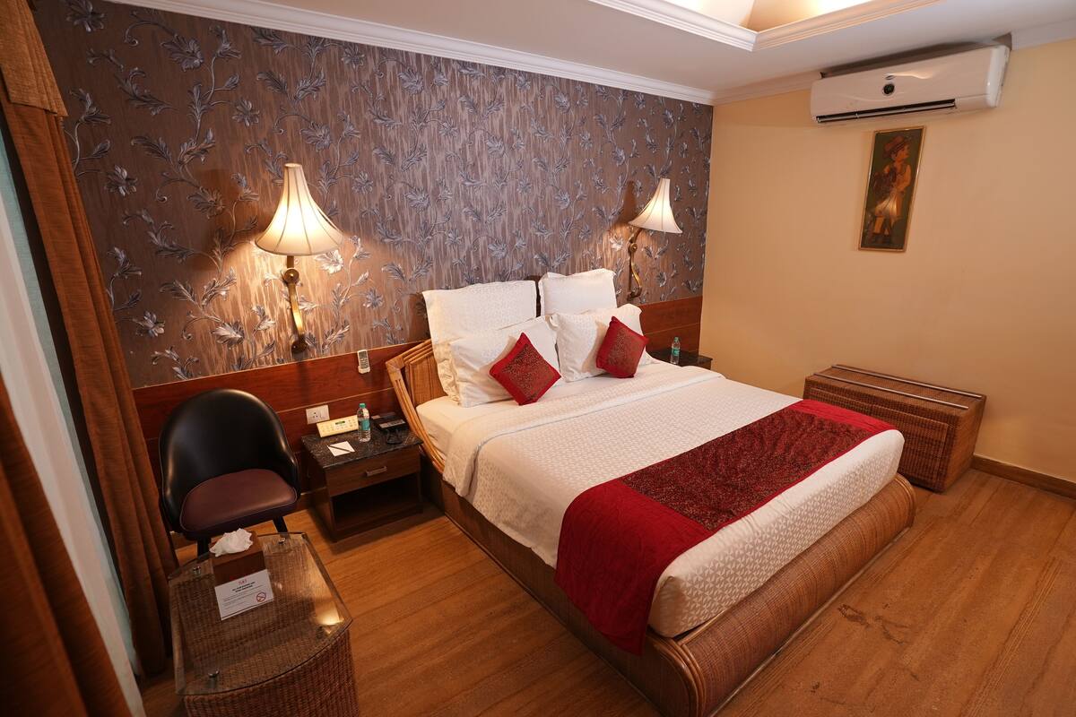 Una habitación de hotel con cama, mesitas de noche, una silla y un escritorio con lámpara.