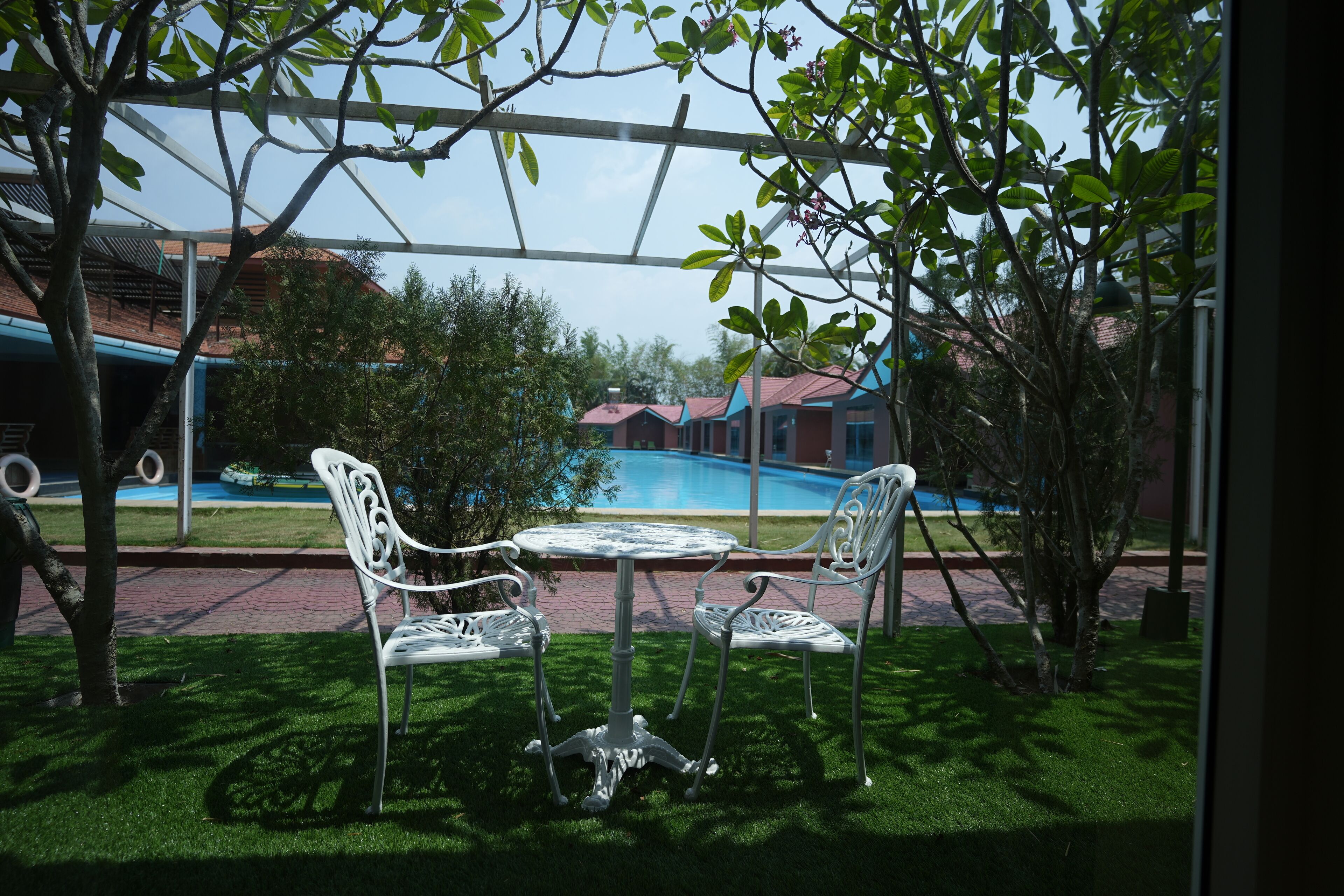 Un espace extérieur aménagé avec une table et des chaises, une piscine en arrière-plan et un bâtiment avec un toit rouge.