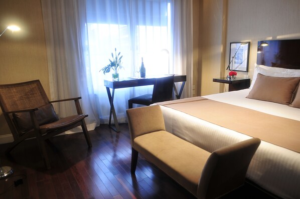 Habitación de hotel con una cama grande, un escritorio con una silla, una mesita con un florero y una lámpara.