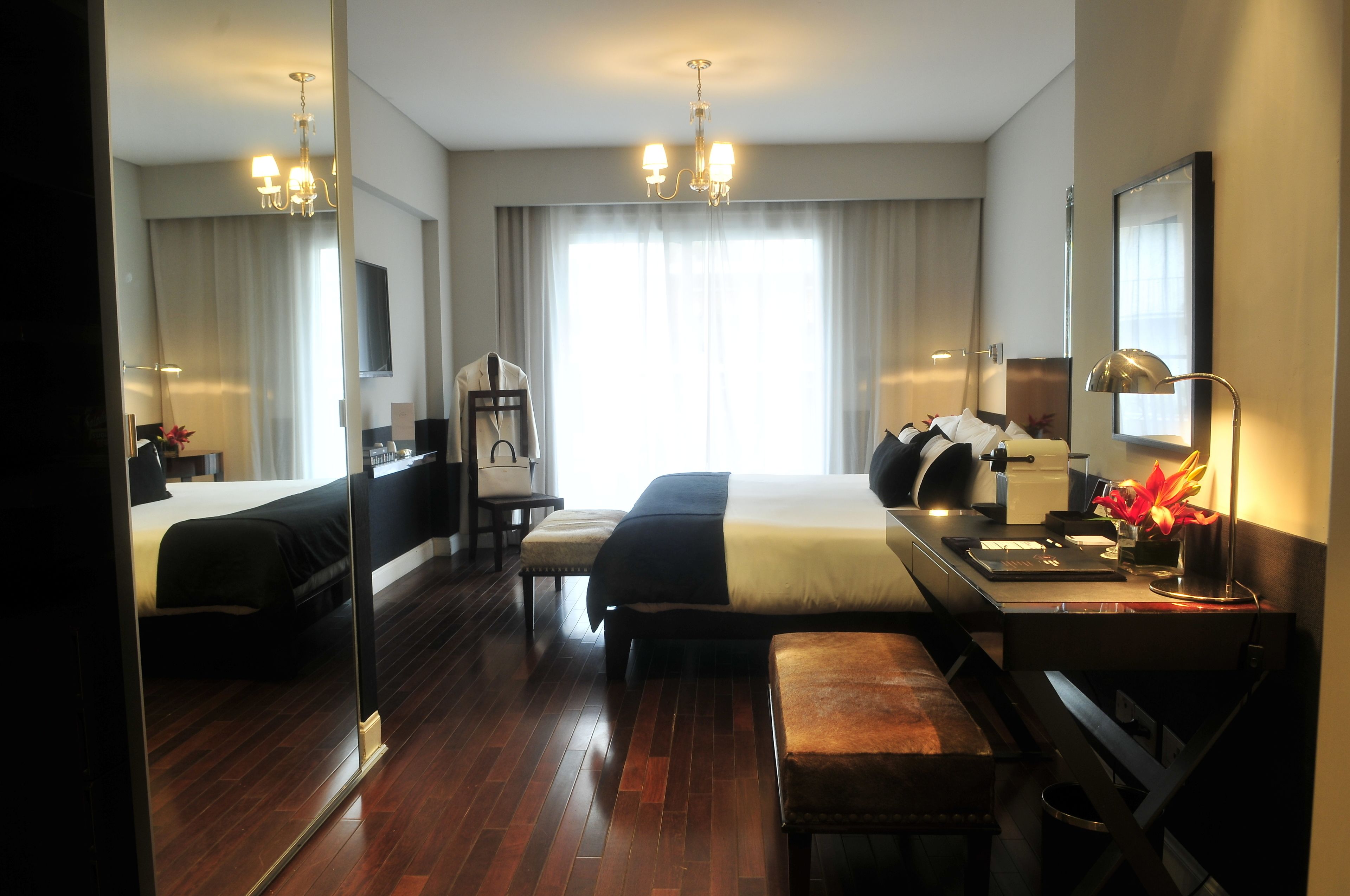 A hotel room with two beds, a desk, a chair, a mirror, and a chandelier.
