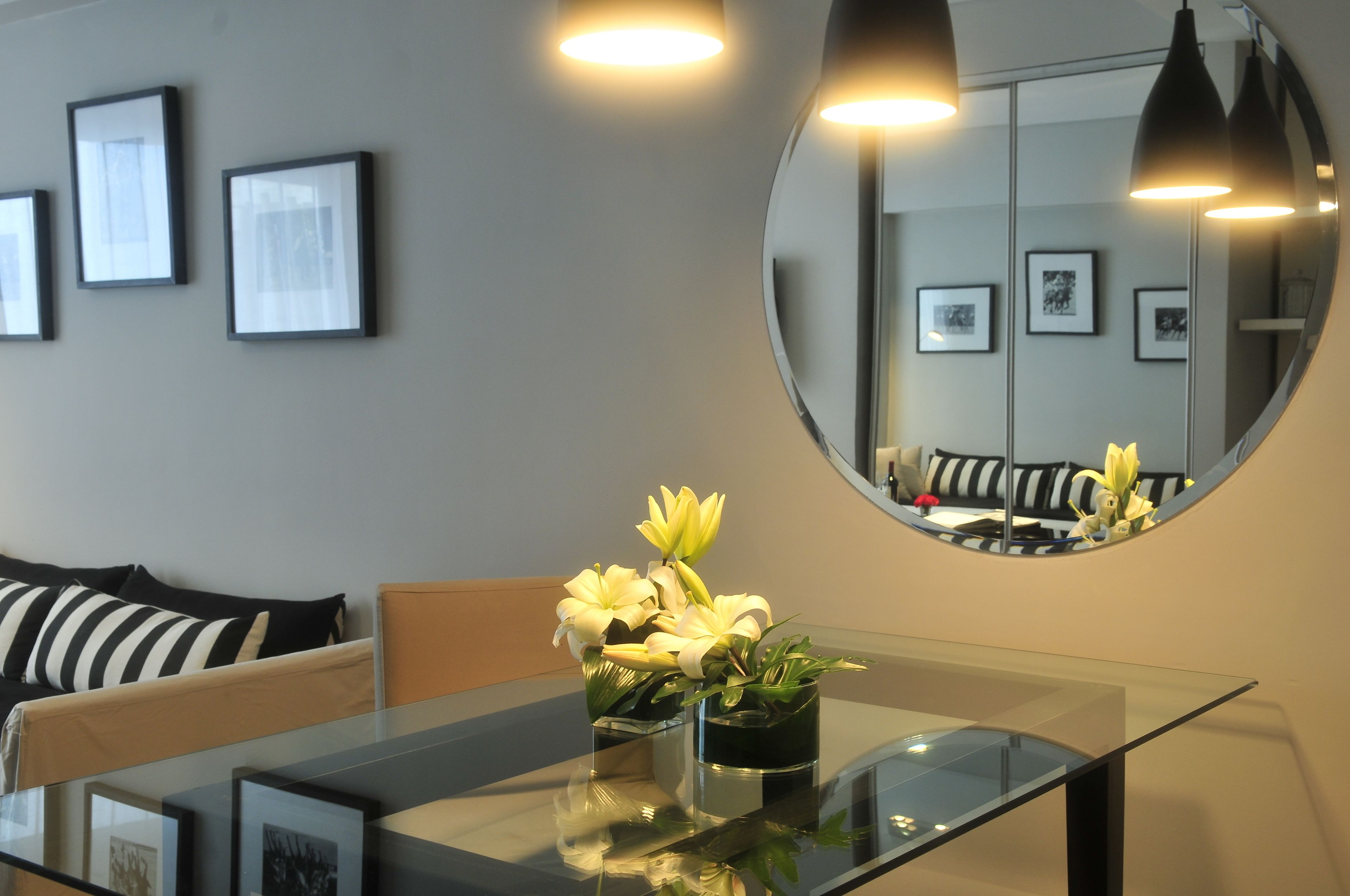 A modern room with a glass table, two vases with flowers, a sofa with striped cushions, and framed pictures on the wall.
