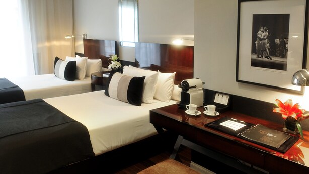 A hotel room with two beds, a desk with a coffee maker, a framed photo, and a vase with flowers. - CasaSur Recoleta (Buenos Aires)