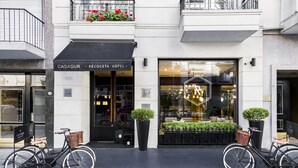 En hotels facade med en sort markise, to cykler med kurve og plantekasser.
