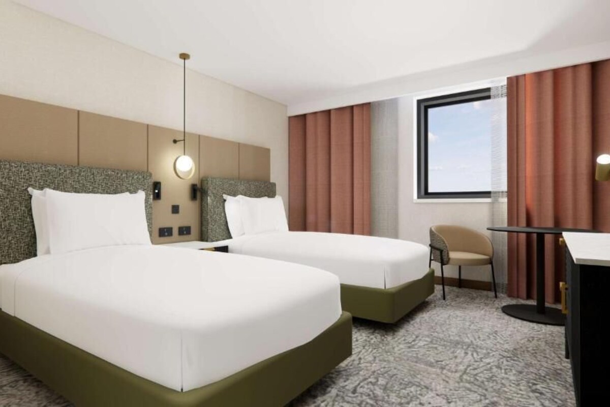 A hotel room with two beds, a desk, a chair, and a large window.