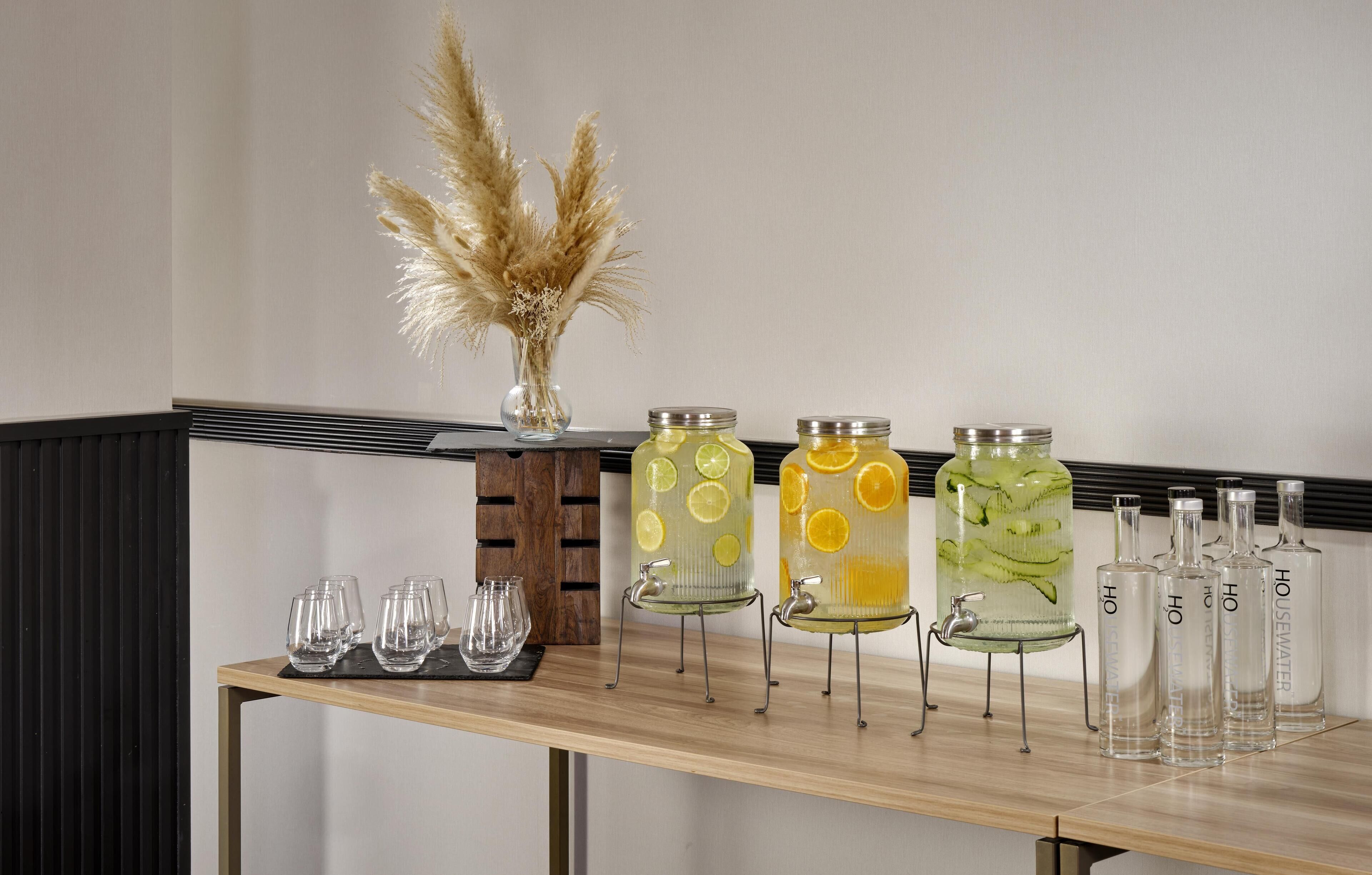 A bar area with a wooden table, clear glasses, and various glass containers with labels.