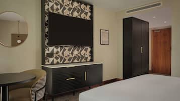 A hotel room with a bed, a desk with a chair, a TV mounted on the wall, a wardrobe, and a door.