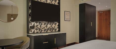 Habitación de hotel con cama, escritorio con silla, televisor montado en la pared, armario y una puerta.