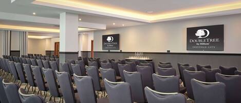 A conference room with rows of chairs, a podium, and a wall-mounted sign for DoubleTree by Hilton Sheffield City.