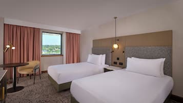A hotel room with two beds, a desk with a chair, a large window with curtains, and a view of the city.