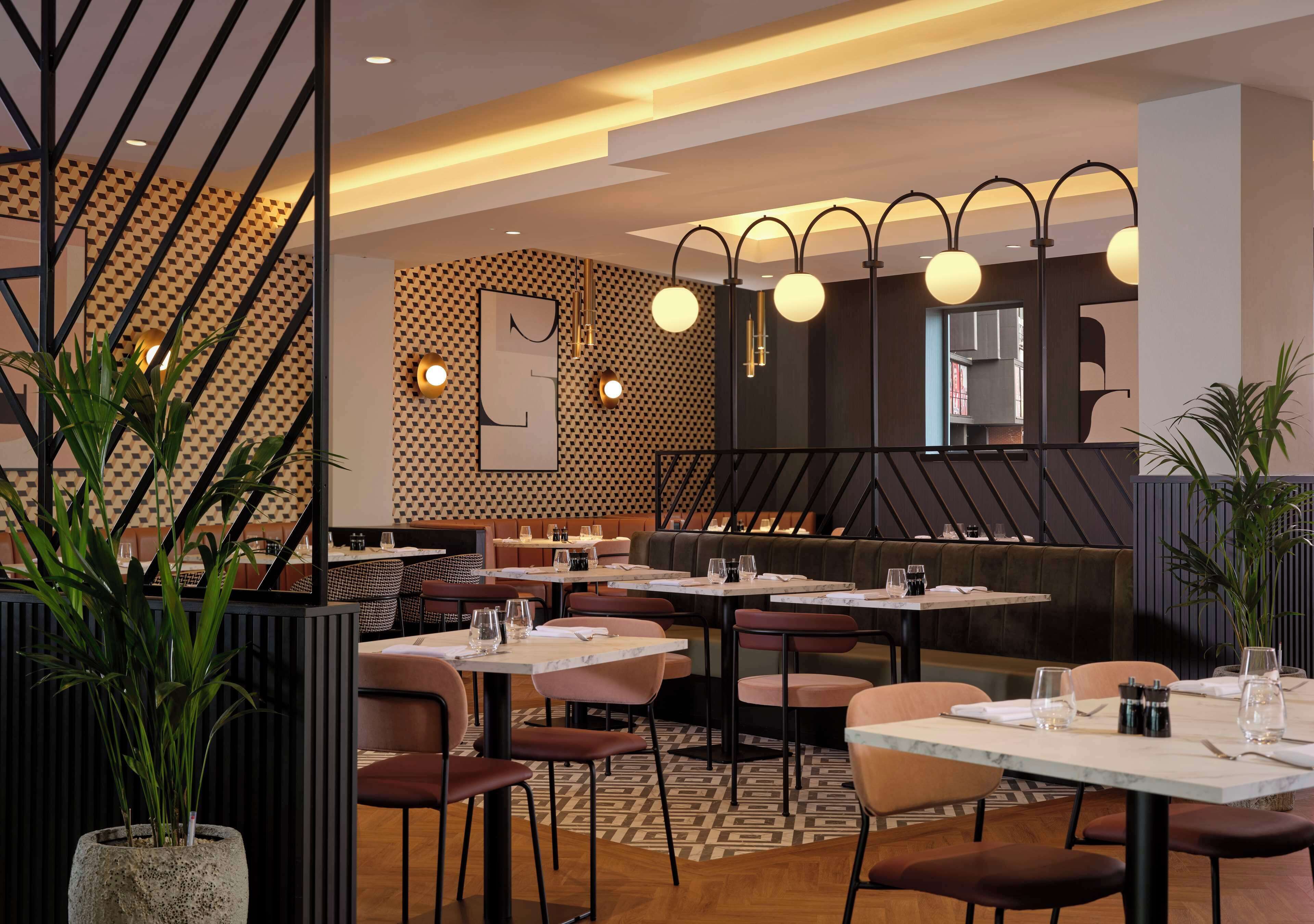 A modern restaurant with a geometric patterned wall, round tables, and cushioned seating.