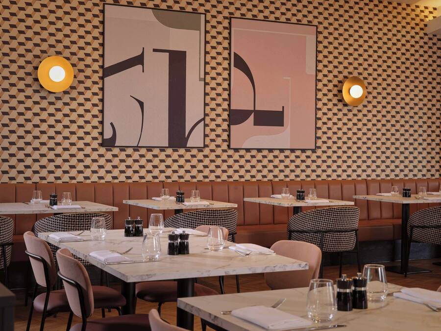 A restaurant with tables and booths, geometric wall art, and wall-mounted lighting.