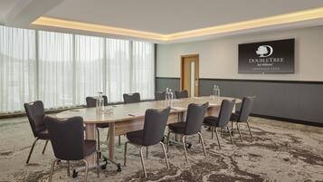 A conference room with a large oval table, six chairs, and a television screen displaying the DoubleTree by Hilton logo.