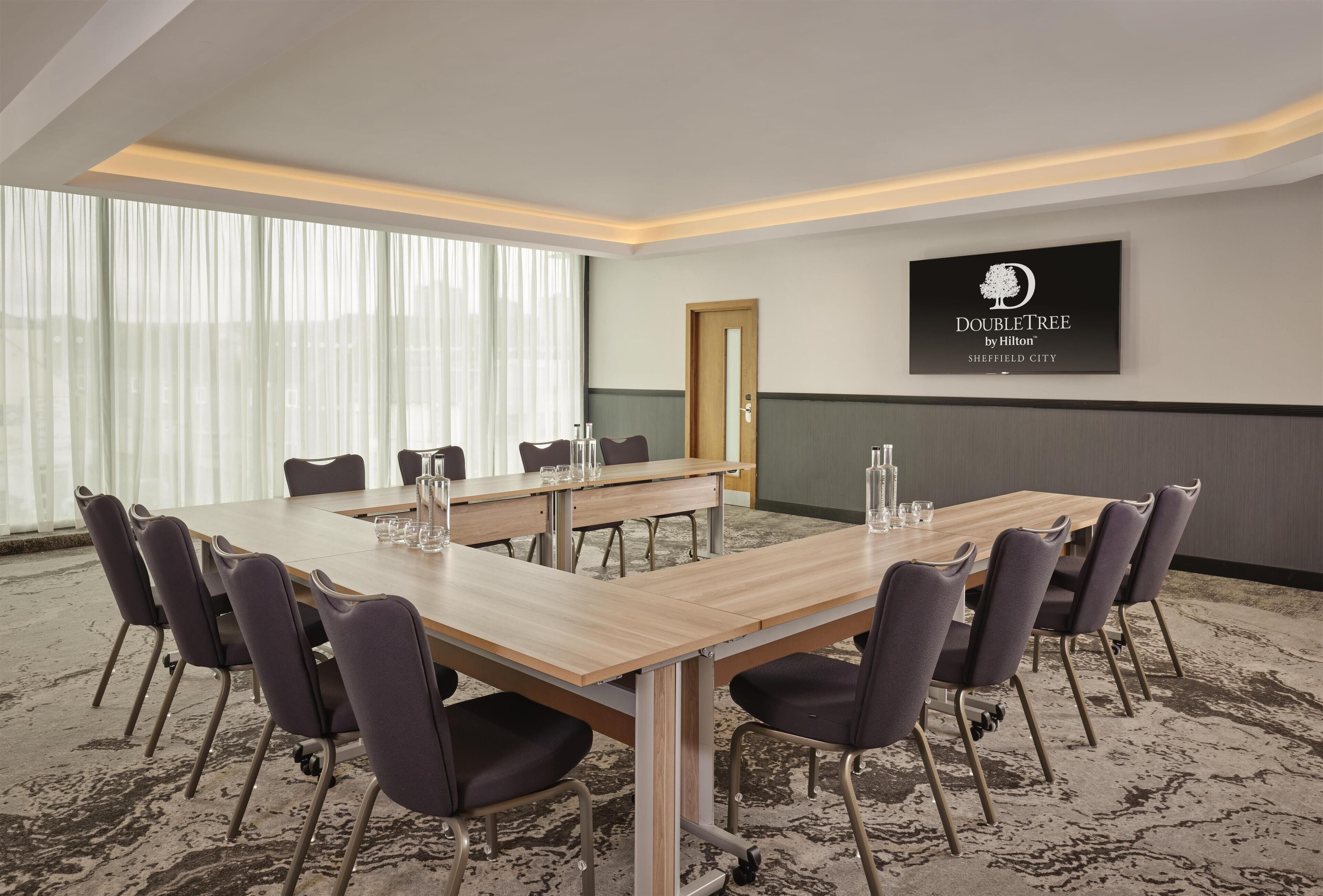 A conference room with a long table, chairs, and a large window with sheer curtains.