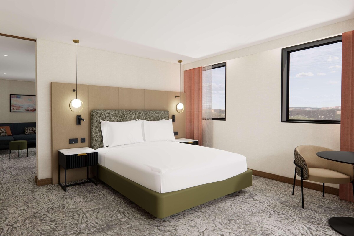 A hotel room with a large bed, a desk, a chair, a sofa, and a window with a view.