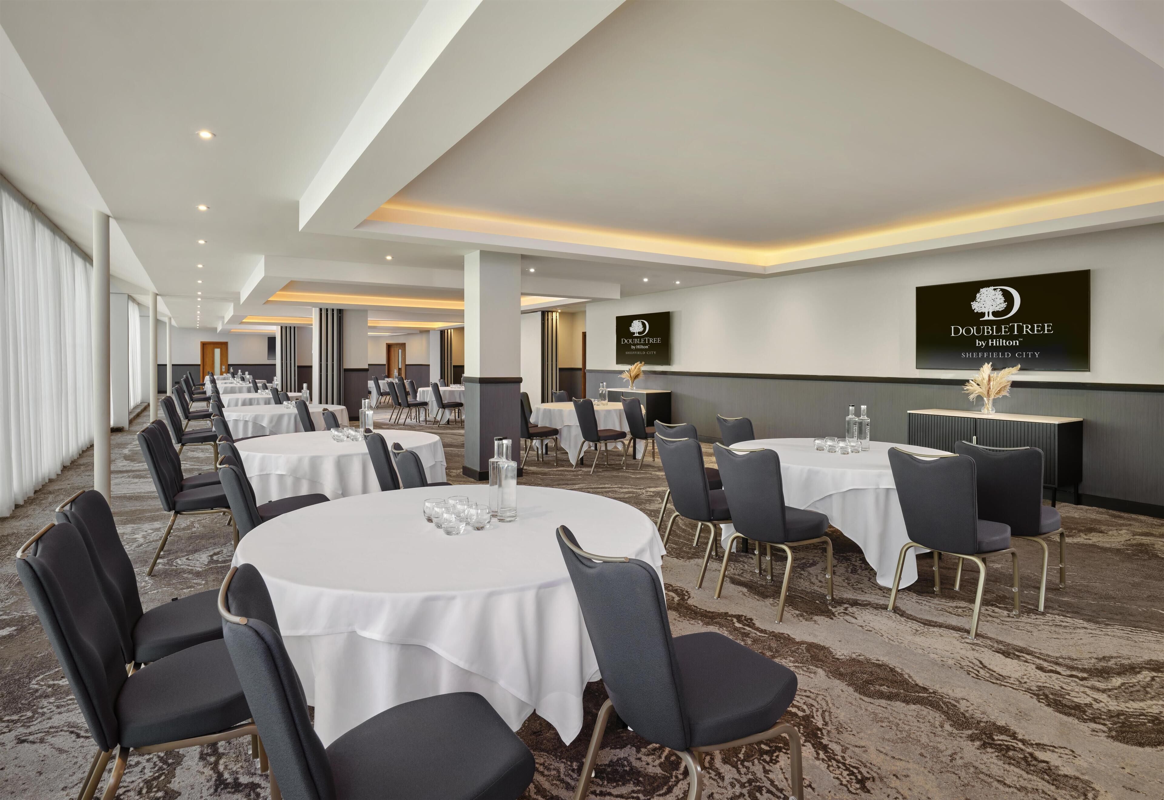 A hotel conference room with round tables, chairs, and a carpeted floor.