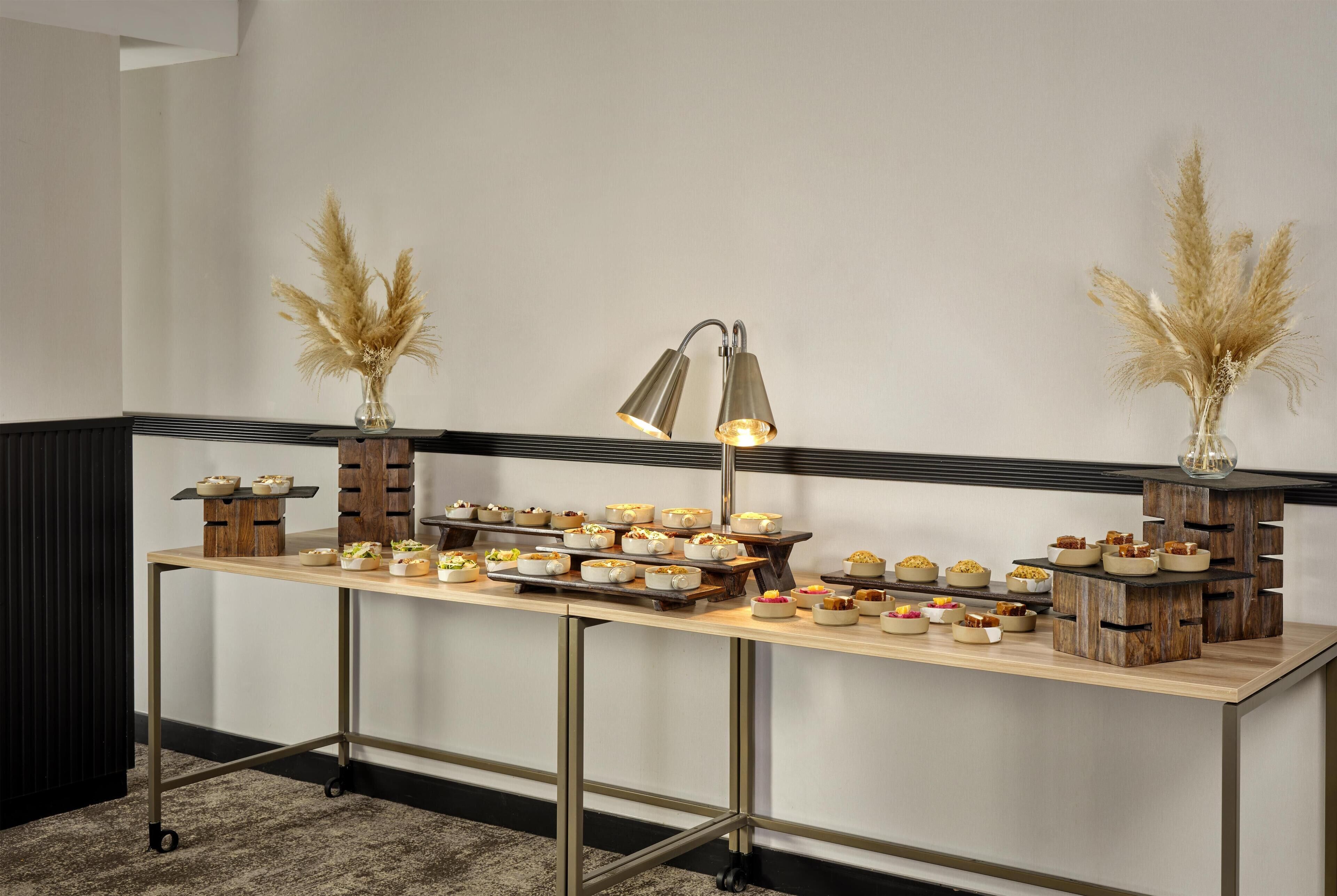 A buffet table with various dishes, a lamp, and decorative pampas grass.