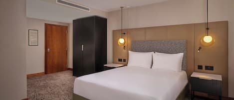 Una habitación de hotel con una cama grande, dos mesitas de noche, un cabecero y piso cubierto de alfombra.