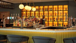 A bar area with multiple taps, a variety of bottles, and a shelf with neatly arranged bottles. - DoubleTree by Hilton Sheffield City (Sheffield)