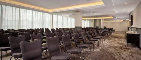A conference room with rows of chairs, large windows, and a carpeted floor.