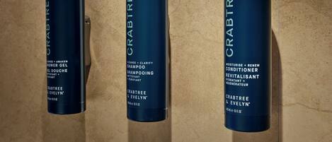 Three bottles of Crabtree & Evelyn hair care products on a tiled wall.