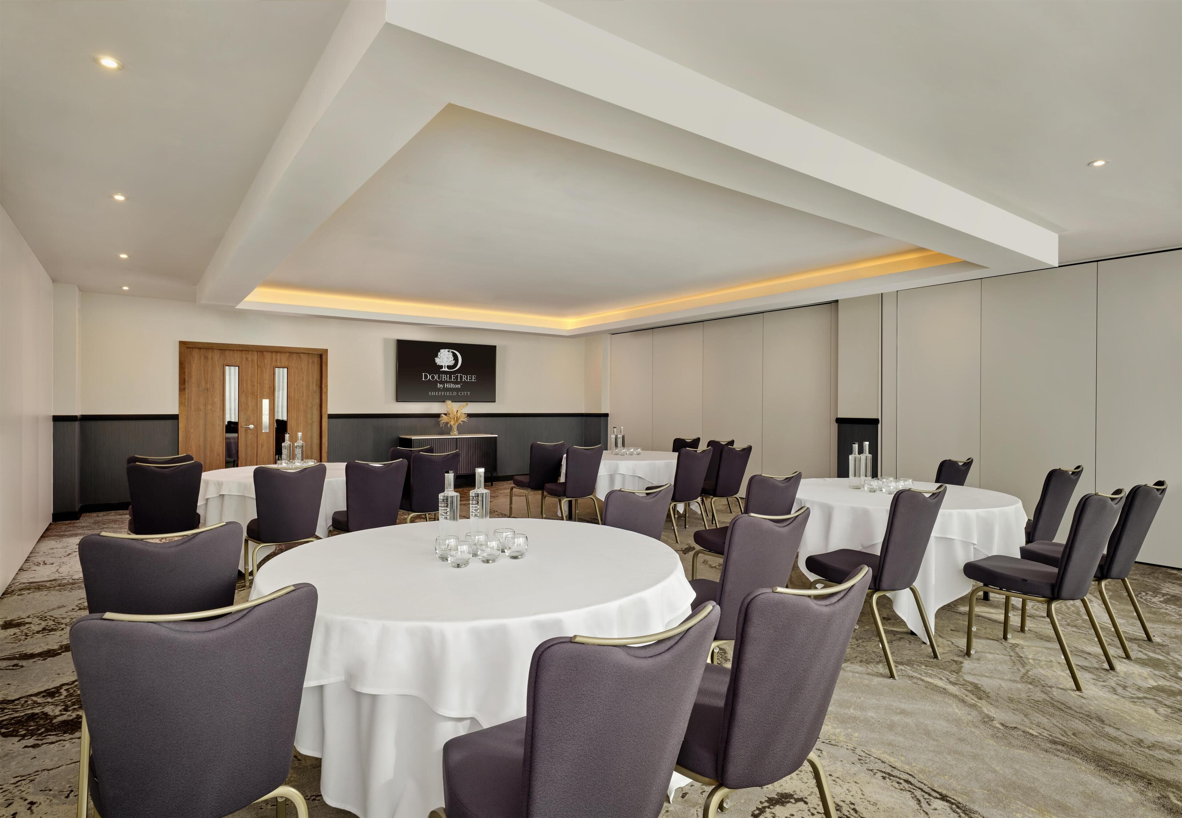 Un salón de conferencias con mesas redondas, sillas y un letrero de 'DOUBLETREE by Hilton' en la pared.