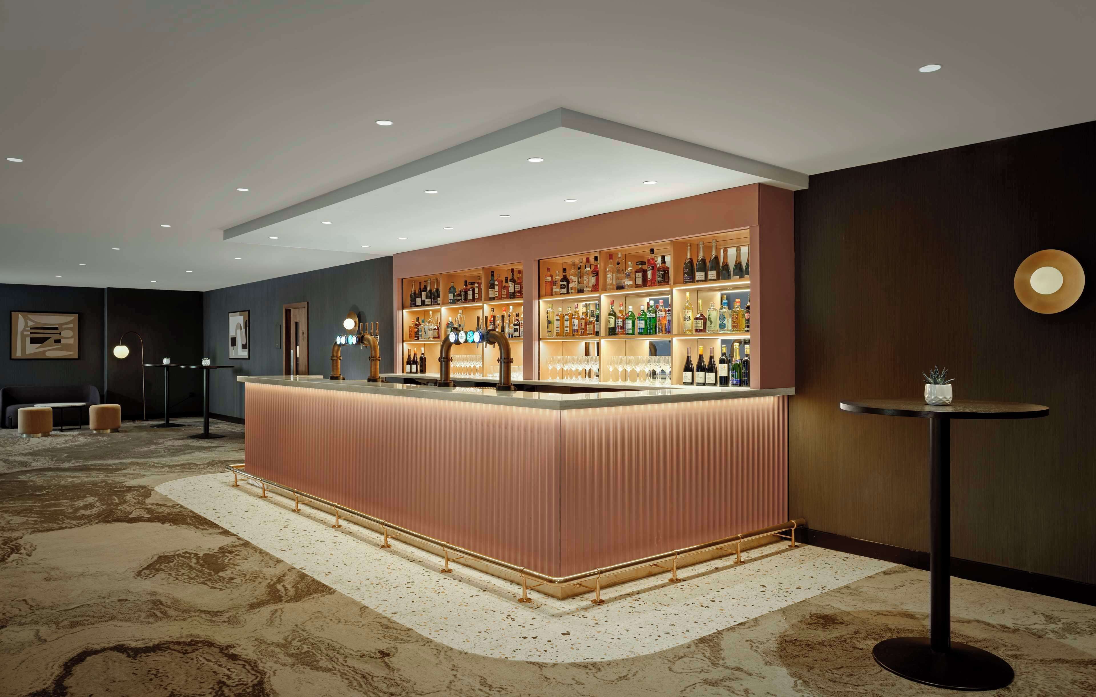 A bar area with a central counter, shelves of bottles, and a round table.