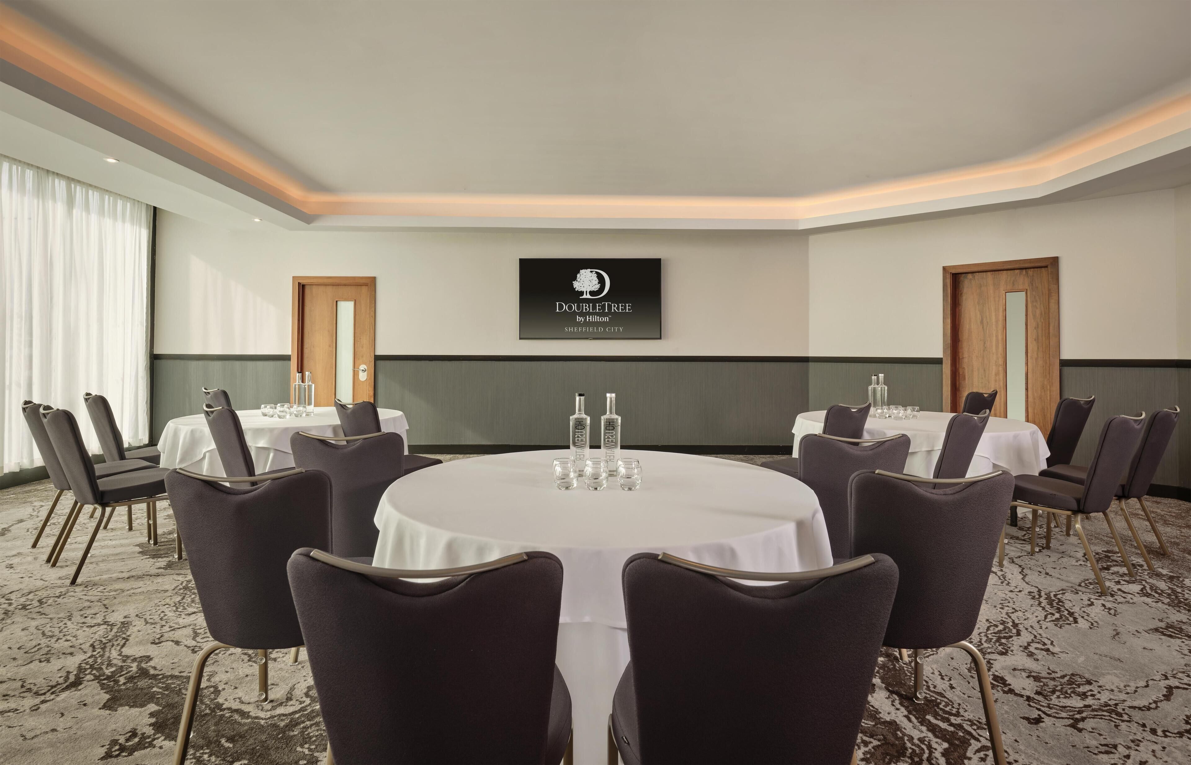 A conference room with a round table, chairs, and a television screen displaying the DoubleTree by Hilton logo.