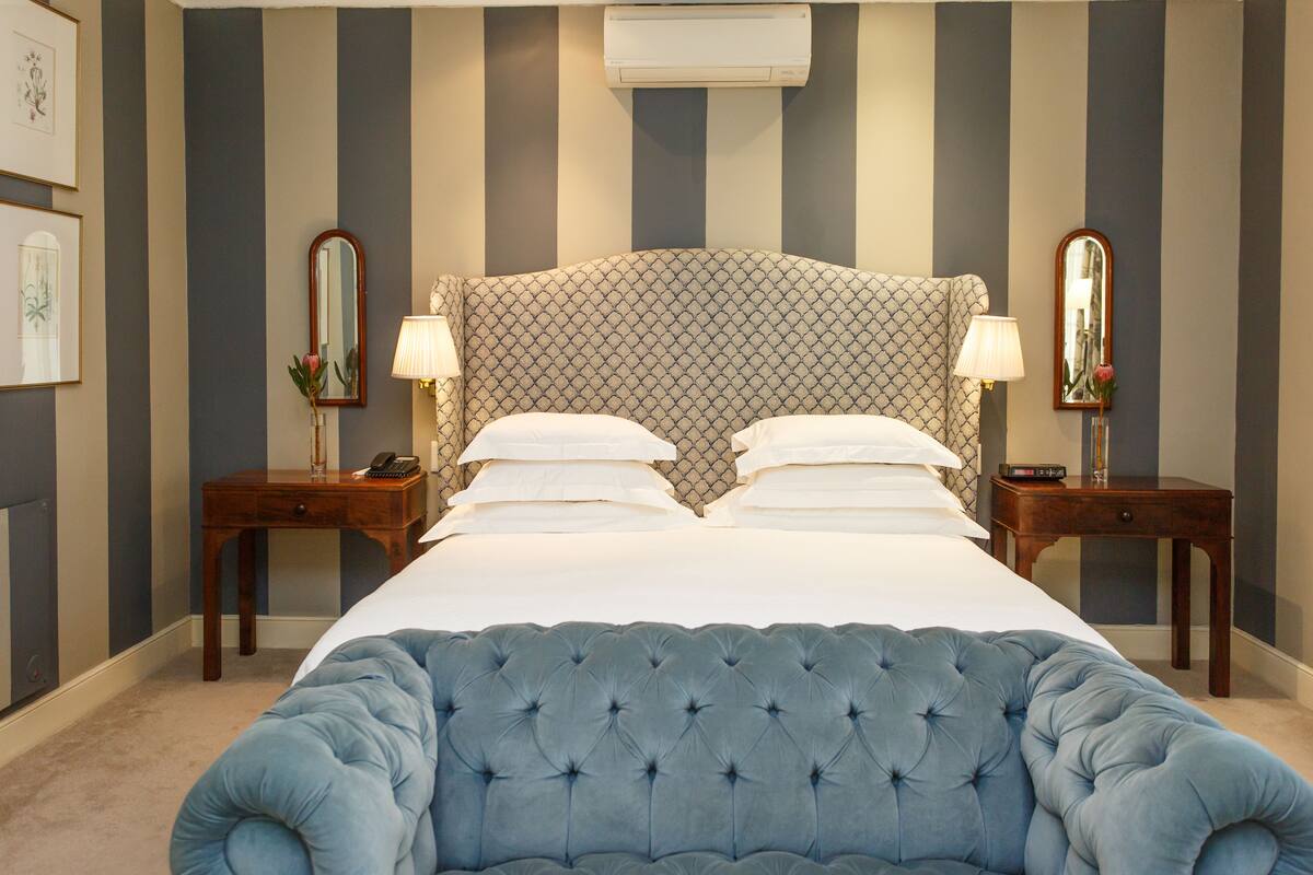 A hotel room with a large bed, two bedside tables, a headboard, and a wall-mounted air conditioner.