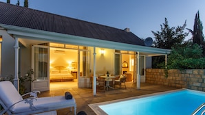A poolside area with lounge chairs, a dining table, and a bedroom with a bed and nightstand. - Rosenhof Boutique Hotel (Oudtshoorn)